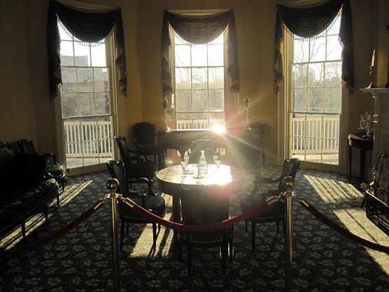The sun casts intense, long rays into the Hamilton Grange Parlor, reflecting on a table and the piano.