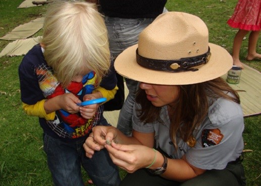 Student looking through a magnifying glass with a ranger. Student looking through a magnifying glass with a ranger.