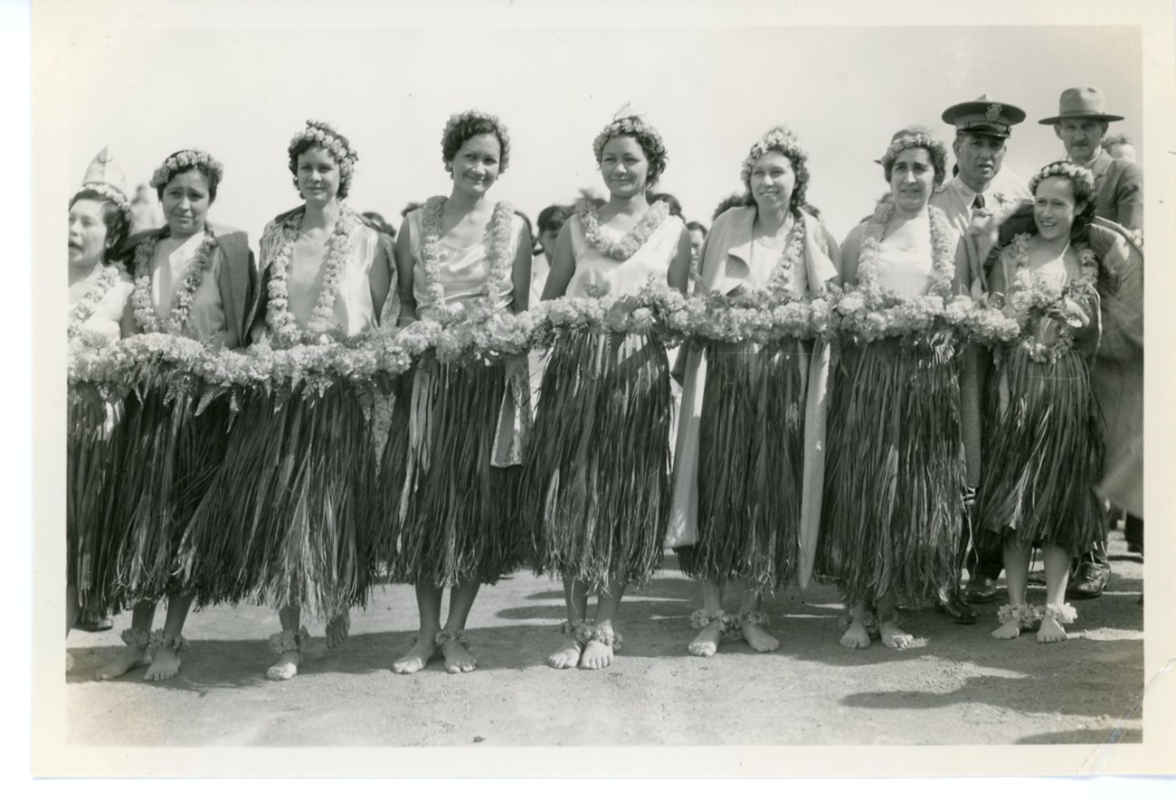 Women wearing grass skirts and holding a lei