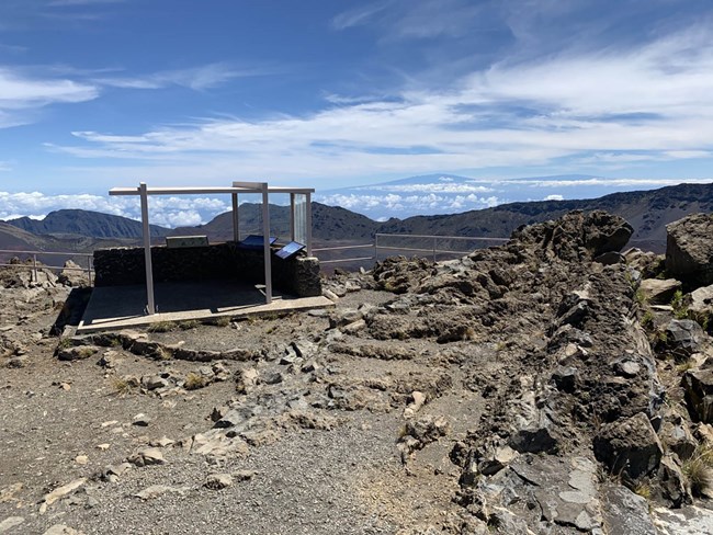 A rocky overlook with metal and glass open air structure on the edge of the crater valley.