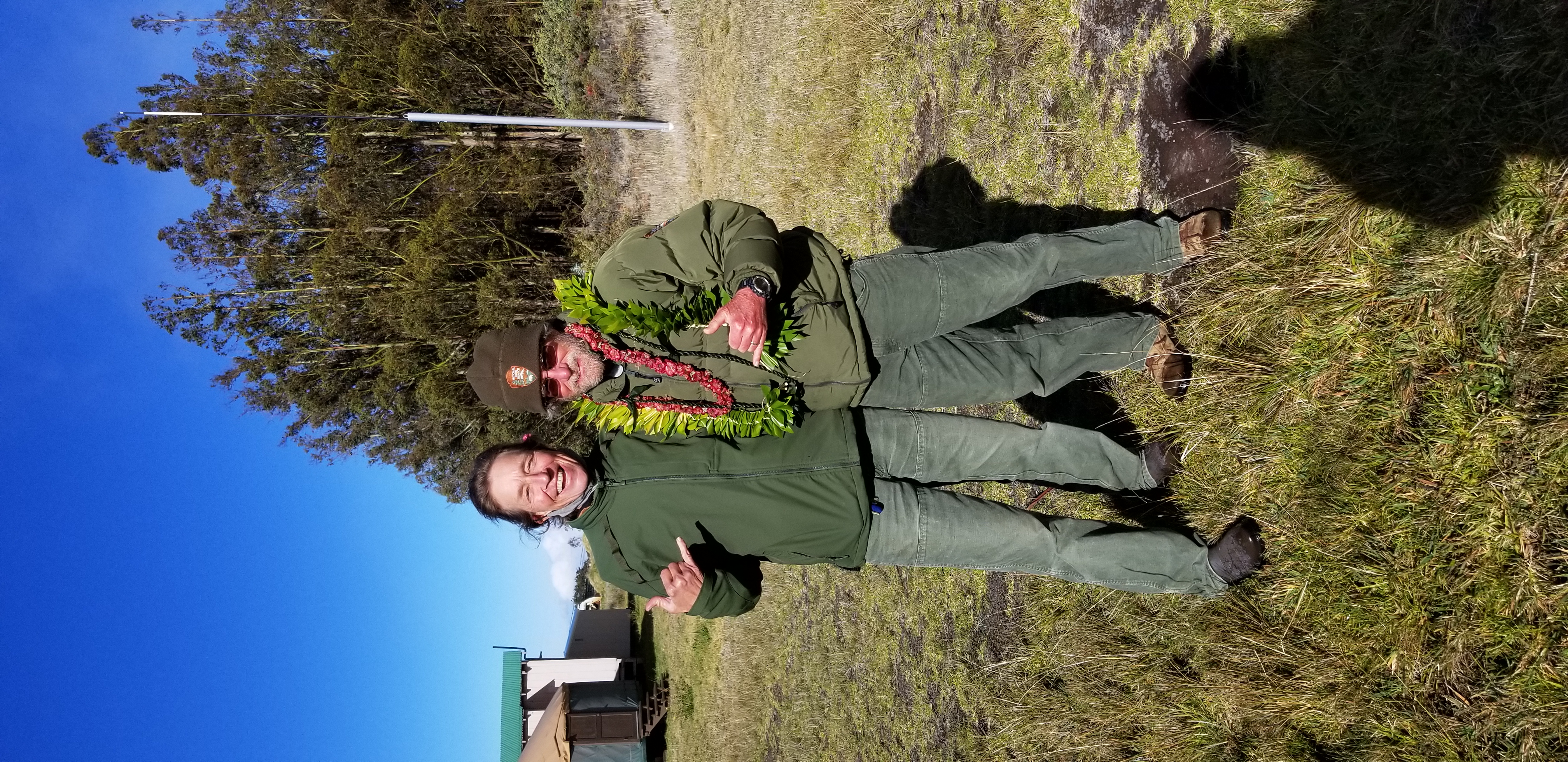 Botanists Patti Welton and Bill Haus at his retirement celebration NPS Photo 1-29-2021 two people stand side by side throwin' shakas, one is adorned with leis around his neck