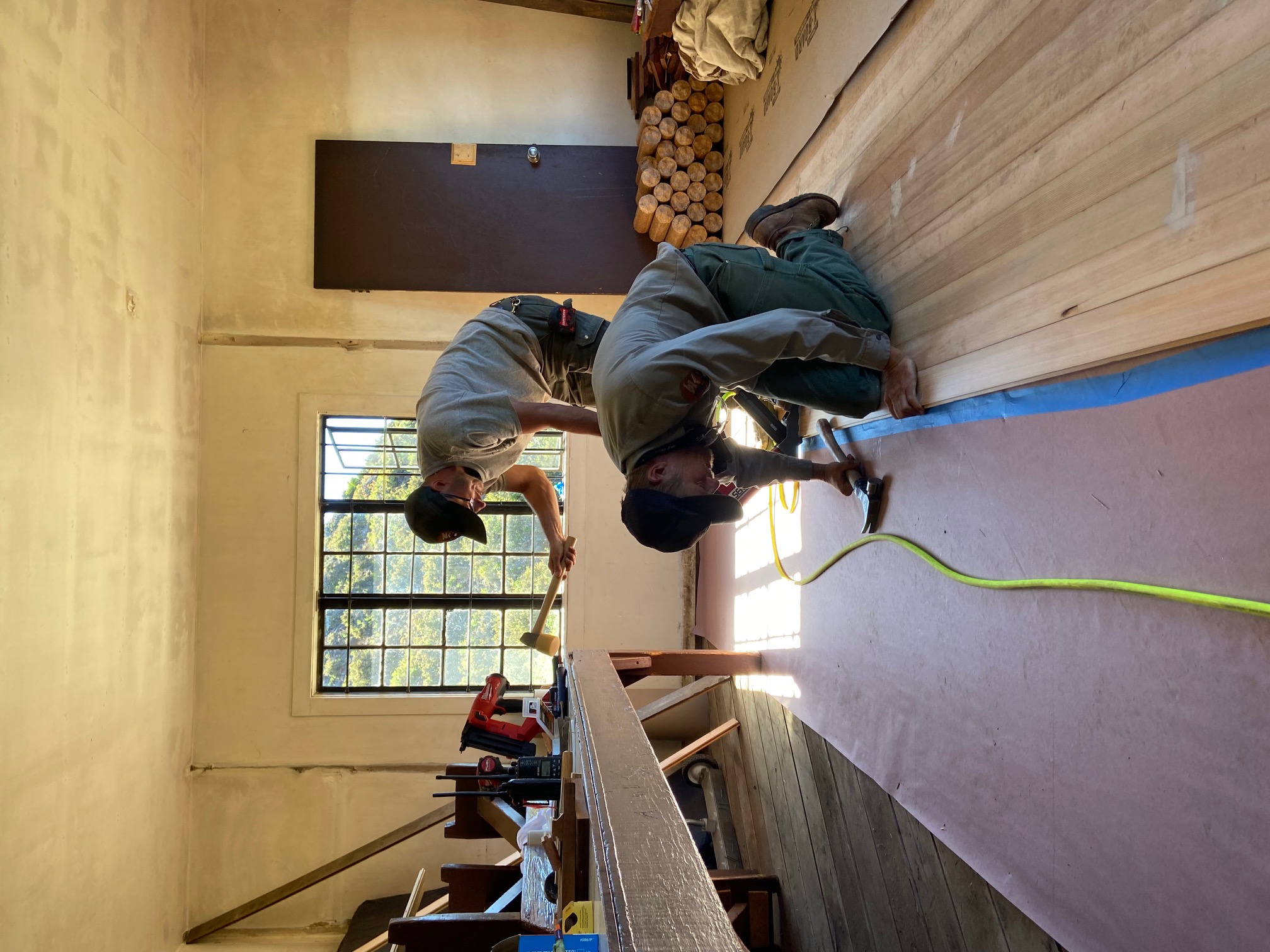 two people work on  replacing floor boards inside a primitive cabin