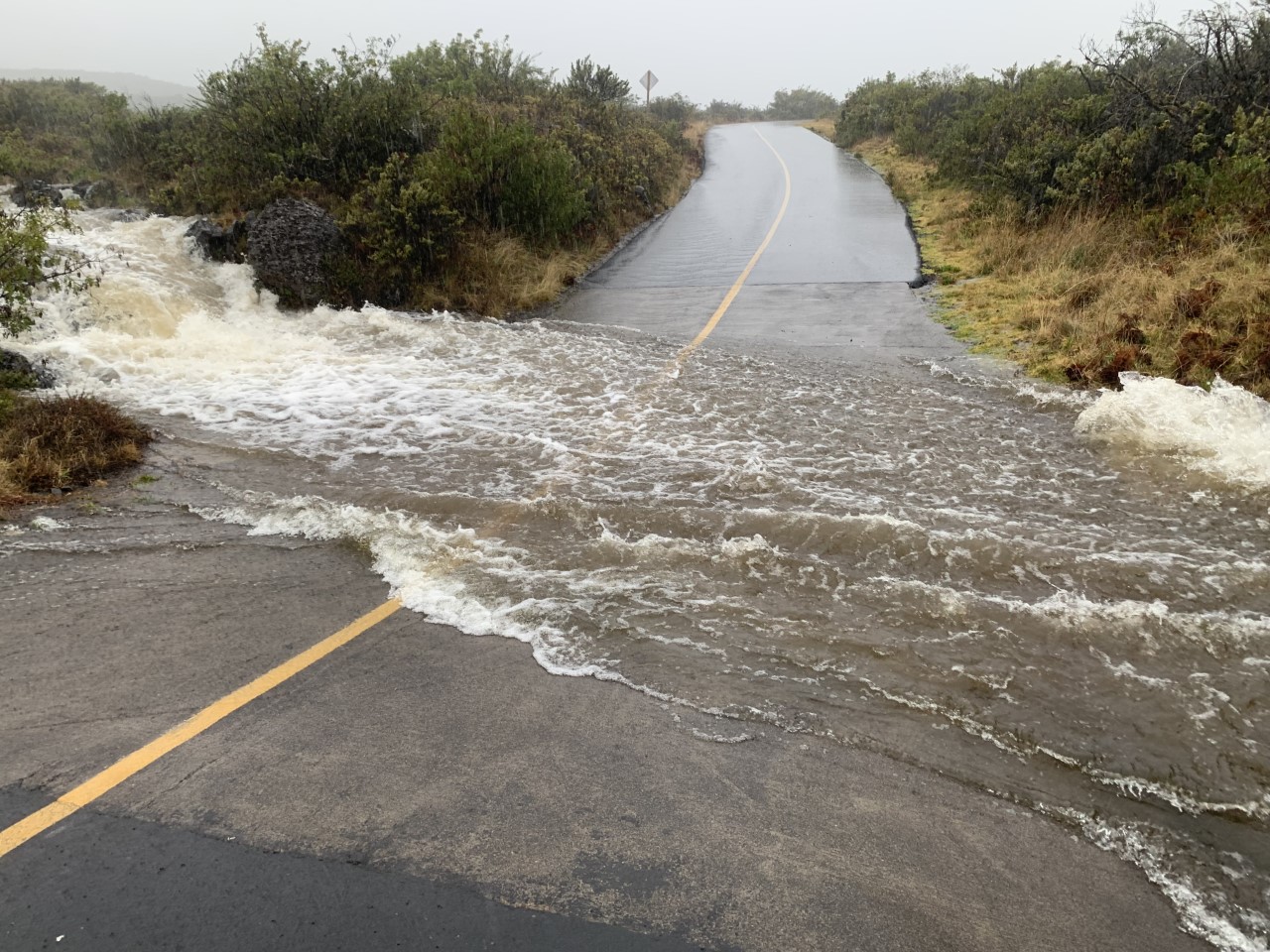 Water several inches deep cascades down to and then flows over a low spot in a two-lane