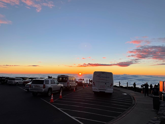 Sunset over a visitor center parking lot as silhouettes of people watch