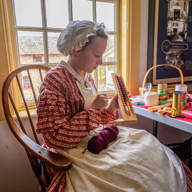 A living historian demonstrates how to use a knitting machine.