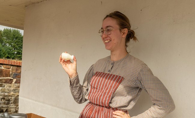 A living historian shakes a jar of cream to demonstrate how to make butter.