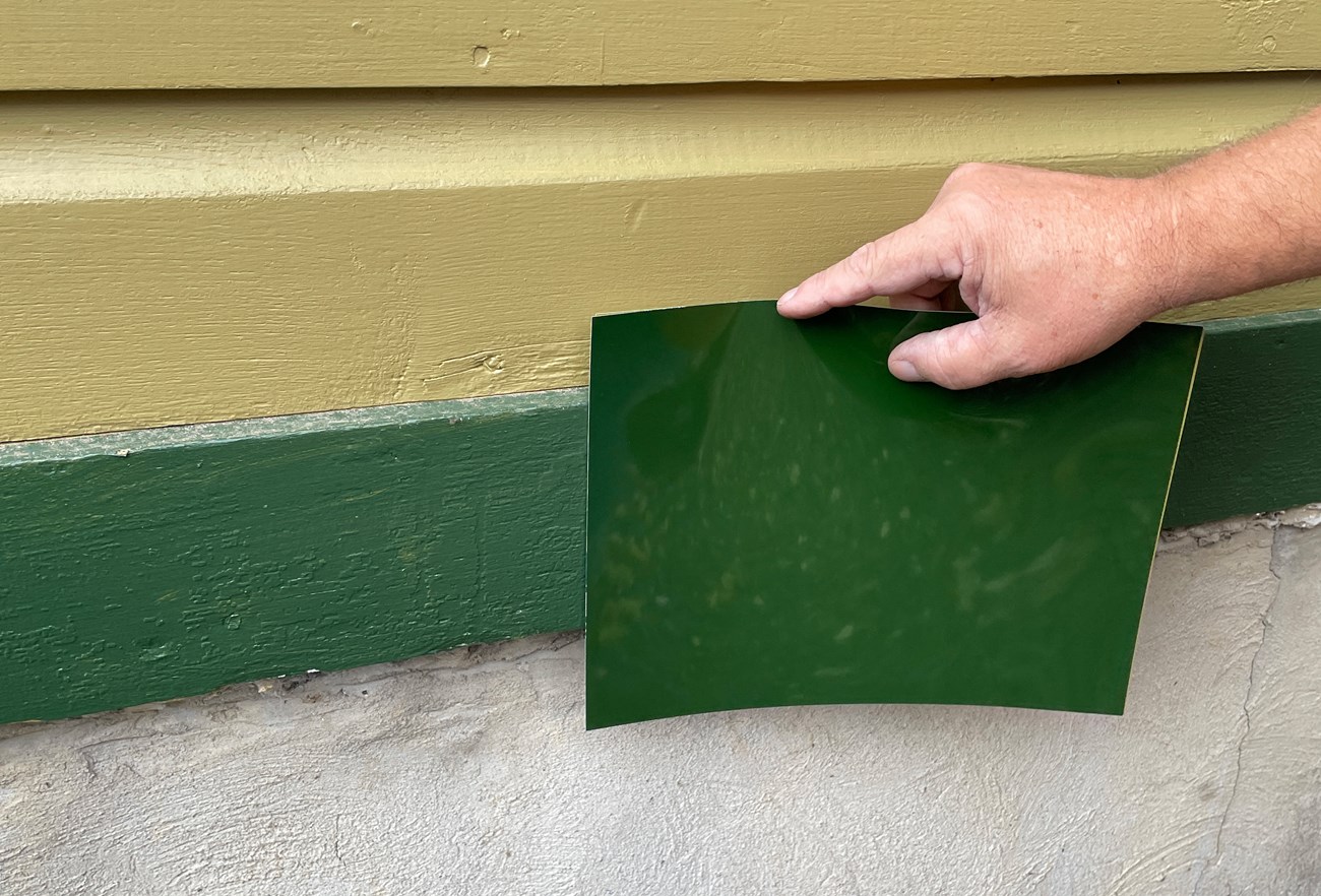 Munsell Sheet showing color difference A green colored plastic sheet held up against green trim. There is a slight difference in the color.
