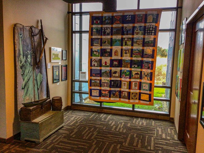 A room with a large quilt and several paintings on the wall.