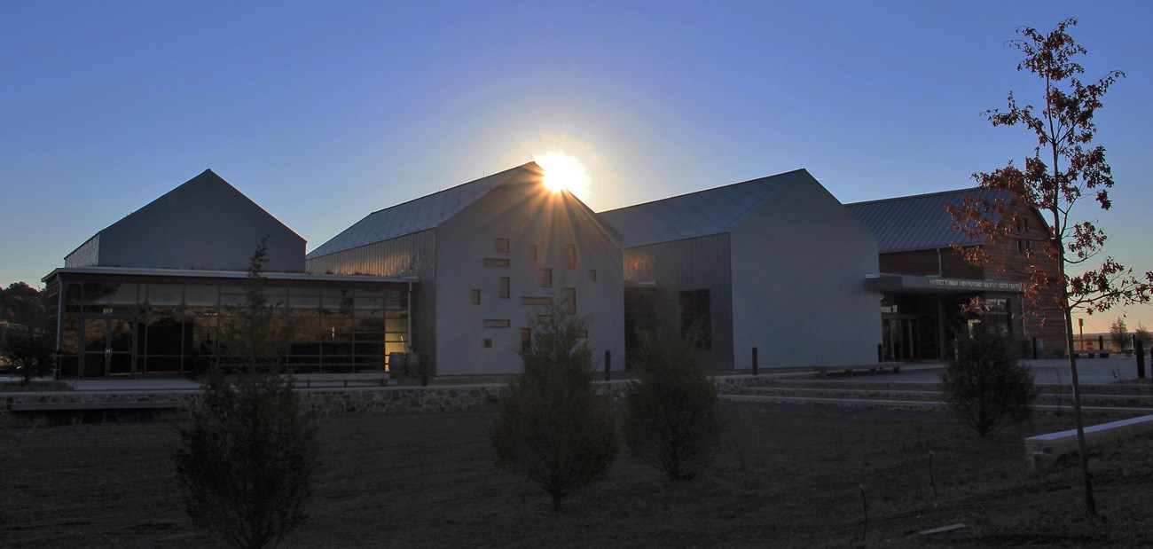 Sun rising above one of four pitched rooftops of the visitor center