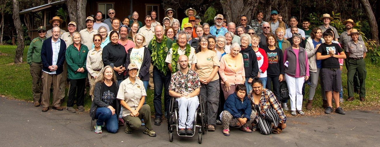 Large diverse group of national park volunteers gathered at the edge of pavement and a grassy area