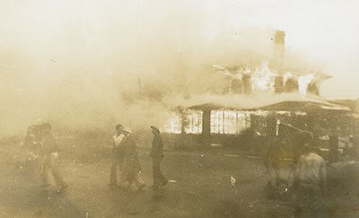 Black and white photo of people walking in front of a burning building