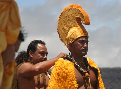 Aliʻi reenactor with a yellow feathered helmet and cape
