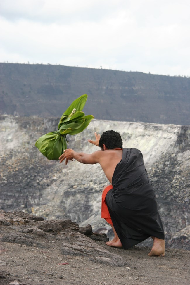 A cultural practitioner throws an offering in a crater