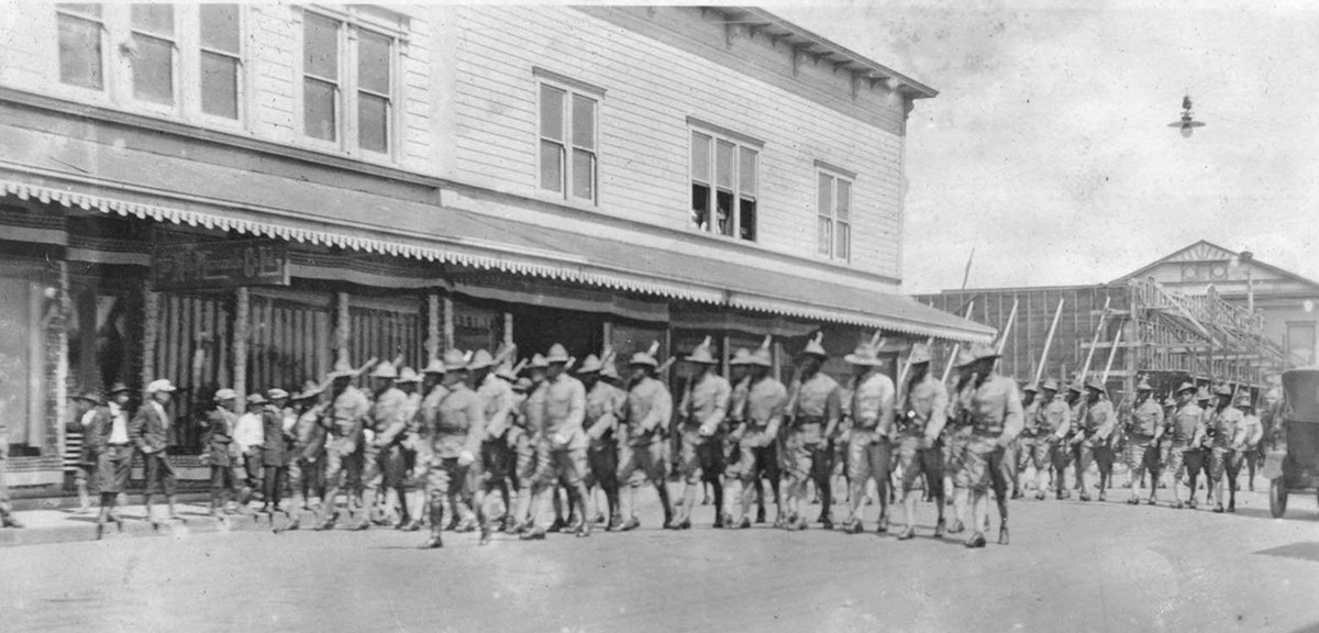 Black and white photo of a company of Black soldiers marching down a city street