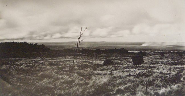 Black and white photo looking down a mountain slope toward a steaming volcanic crater