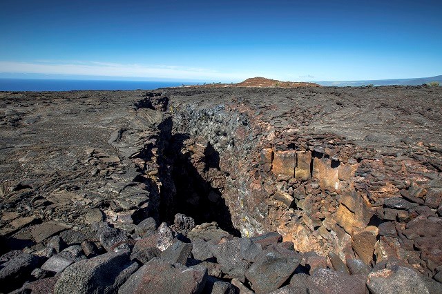 A large volcanic crack with a cinder cone in the background.