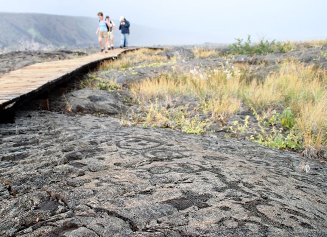 Visitors on a boardwalk over petroglyphs in dark gray rock