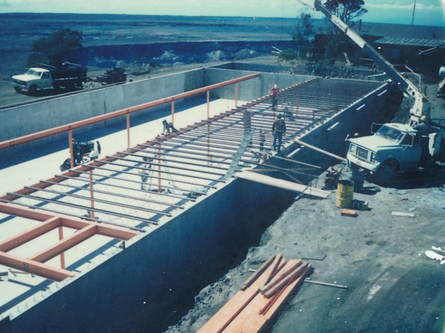 Workers joining metal beams in a basement with small crane overhead.