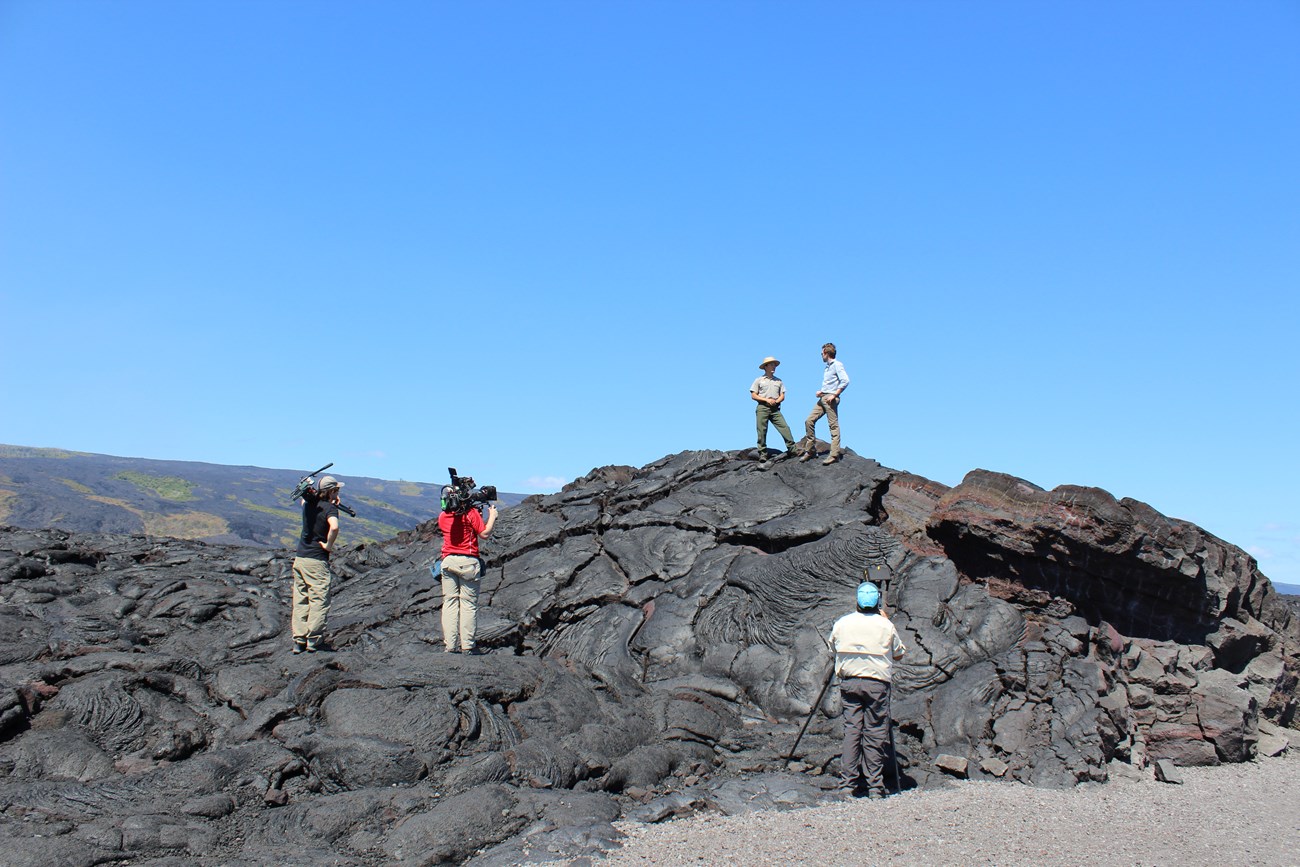 Ranger standing on hardened lava is interviewed by Philippe Cousteau, Jr. for a television show.