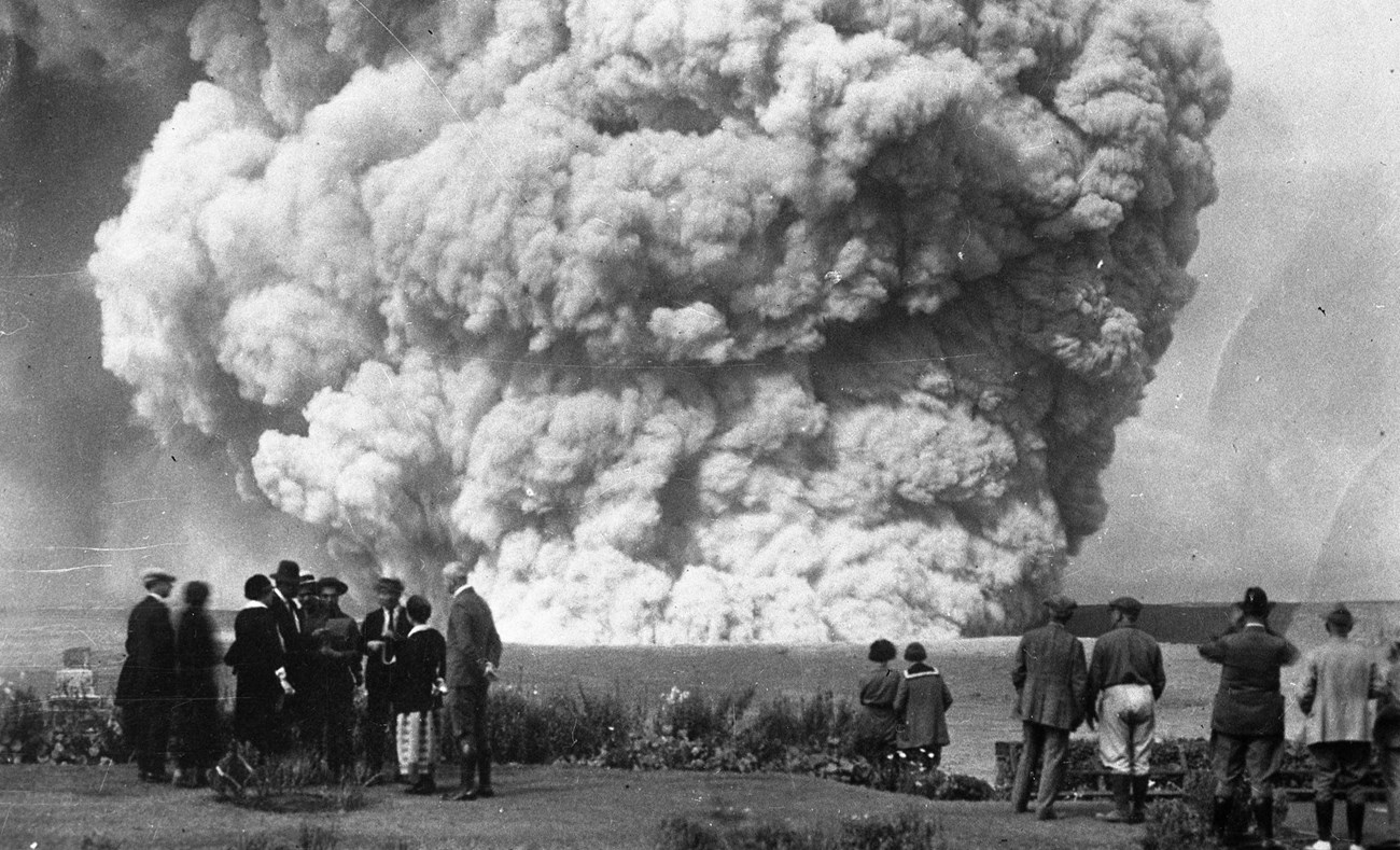 Human figures standing in front of a plume emanating from a crater