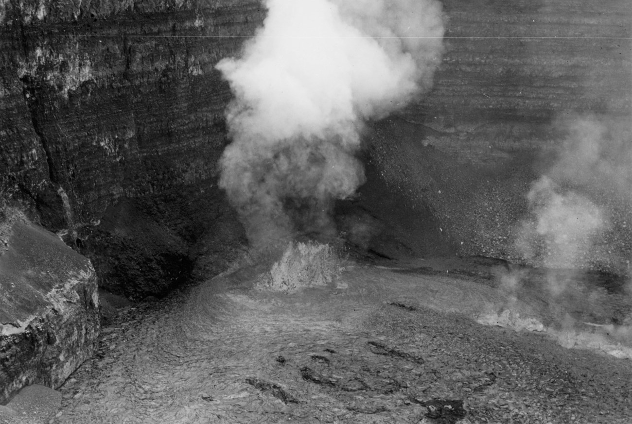 Black and white image of a lava fountain along the bottoms of a crater wall.