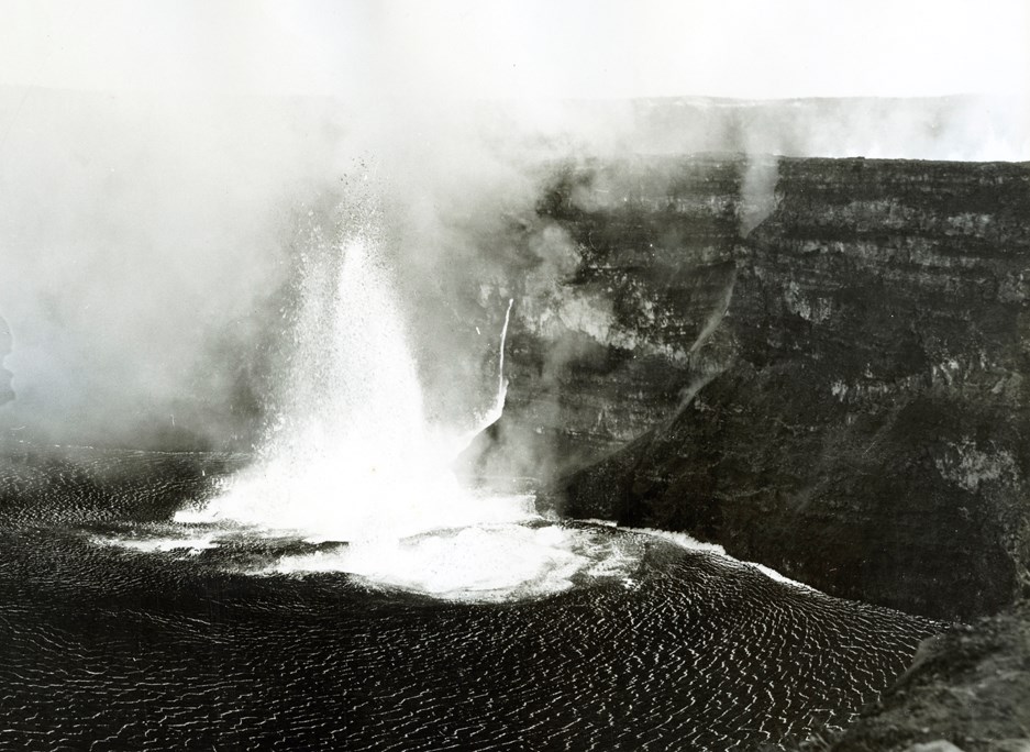 Black and white image of a lava fountain along the bottoms of a crater wall.