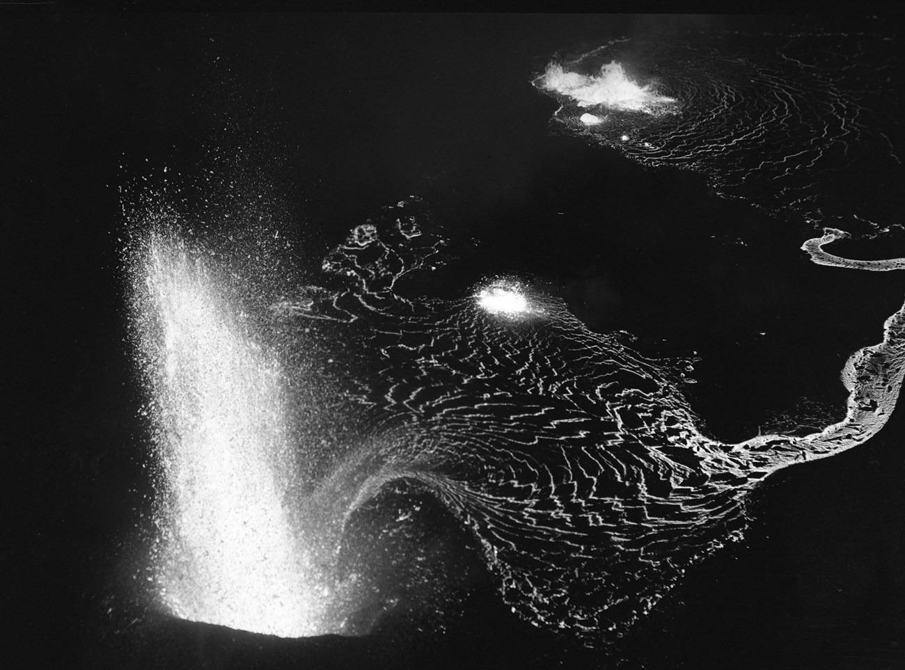 Black and white photo of a lava fountain and lava river at night from above