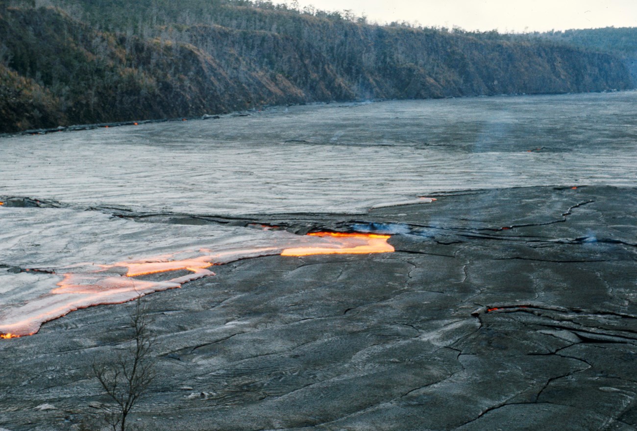 Glowing orange molten lava flow on the floor of a caldera with forested walls