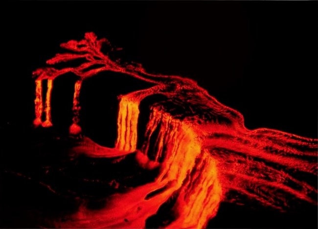 Aerial nighttime view of a molten lava flow cascading into a crater