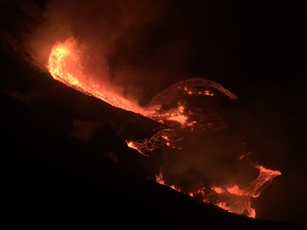 Lava cascading down into a crater at night, viewed from above