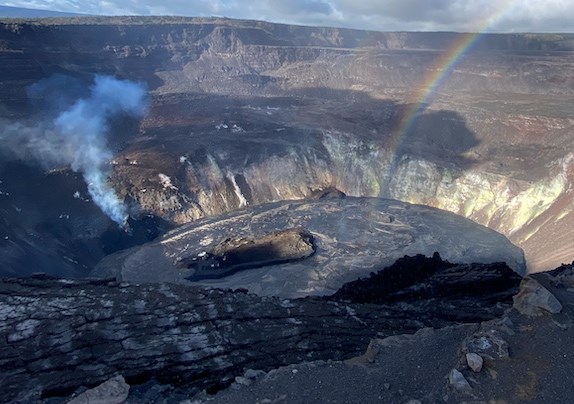 Rainbow rising from a black lake of molten lava within a volcanic crater