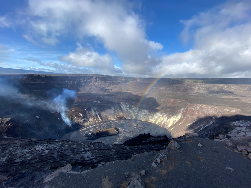 Lake of molten lava in a volcanic crater under blue sky with white clouds and a rainbow
