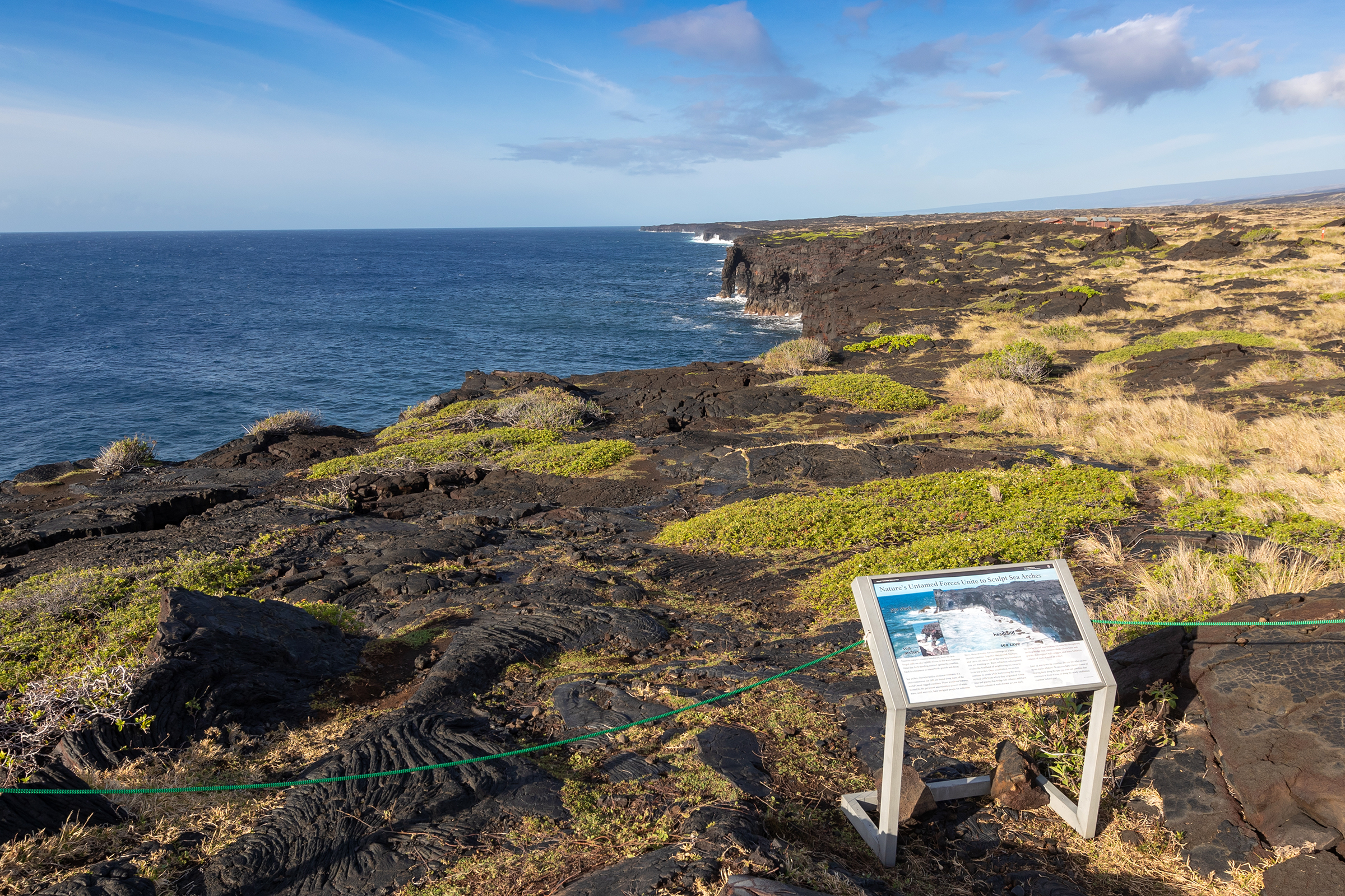 Sea cliffs, a wayside exhibit, and a distant sea arch