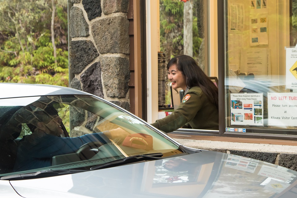 A park ranger in a booth accepts a credit card from a park visitor inside his vehicle