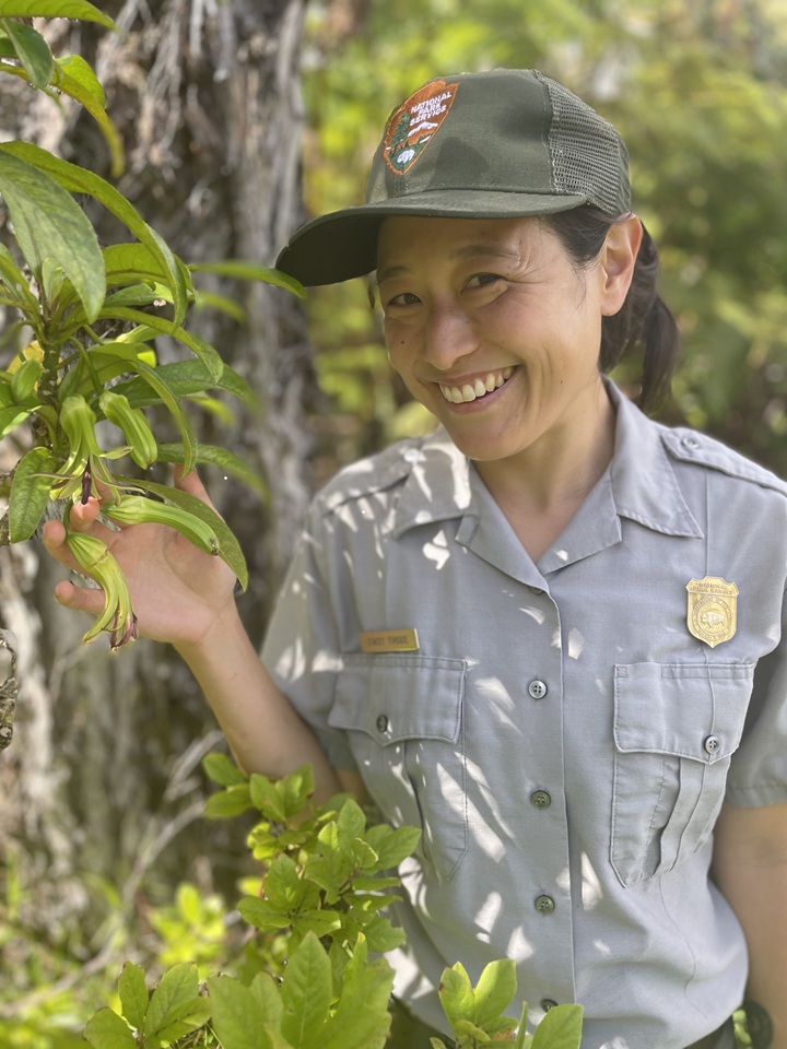 A female park ranger stands next to a blooming plant