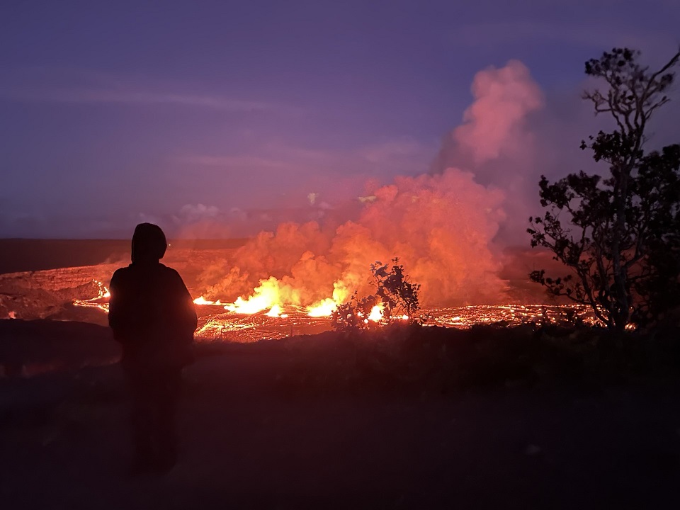 A person observes a lava lake with fountains in darkness