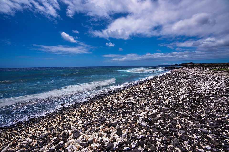 960-HAVO_20240901_Kahakahakea-Beach-1_J.Wei White coral fragements and black lava rock pebbles form a beach with small waves lapping the shore