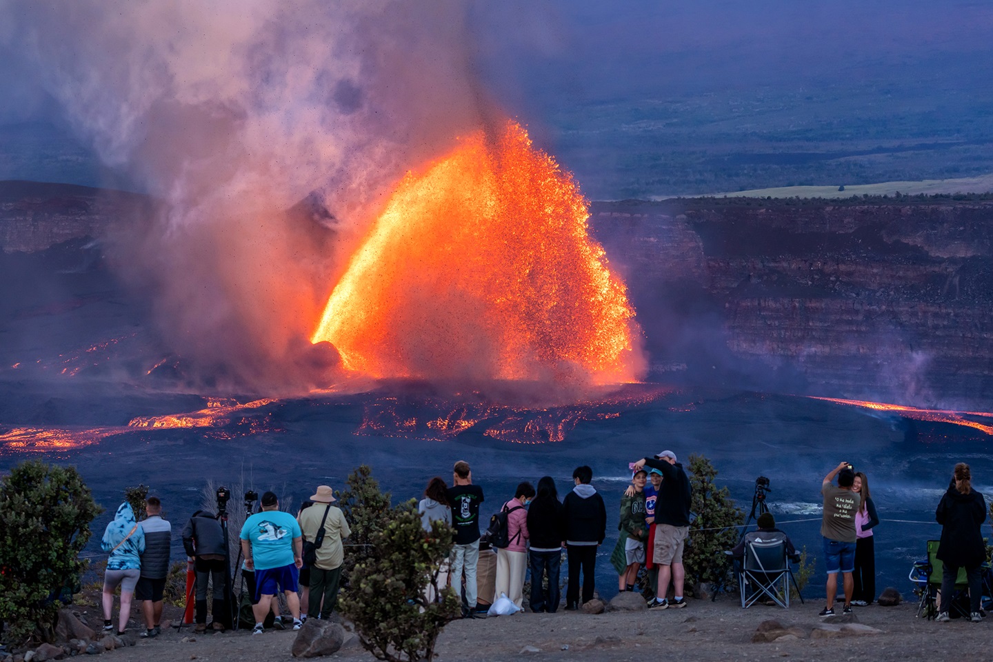 Visitors watch from a distance as Kīlauea volcano erupts with a dramatic arcing fountain of lava in Hawaiʻi Volcanoes National Park.