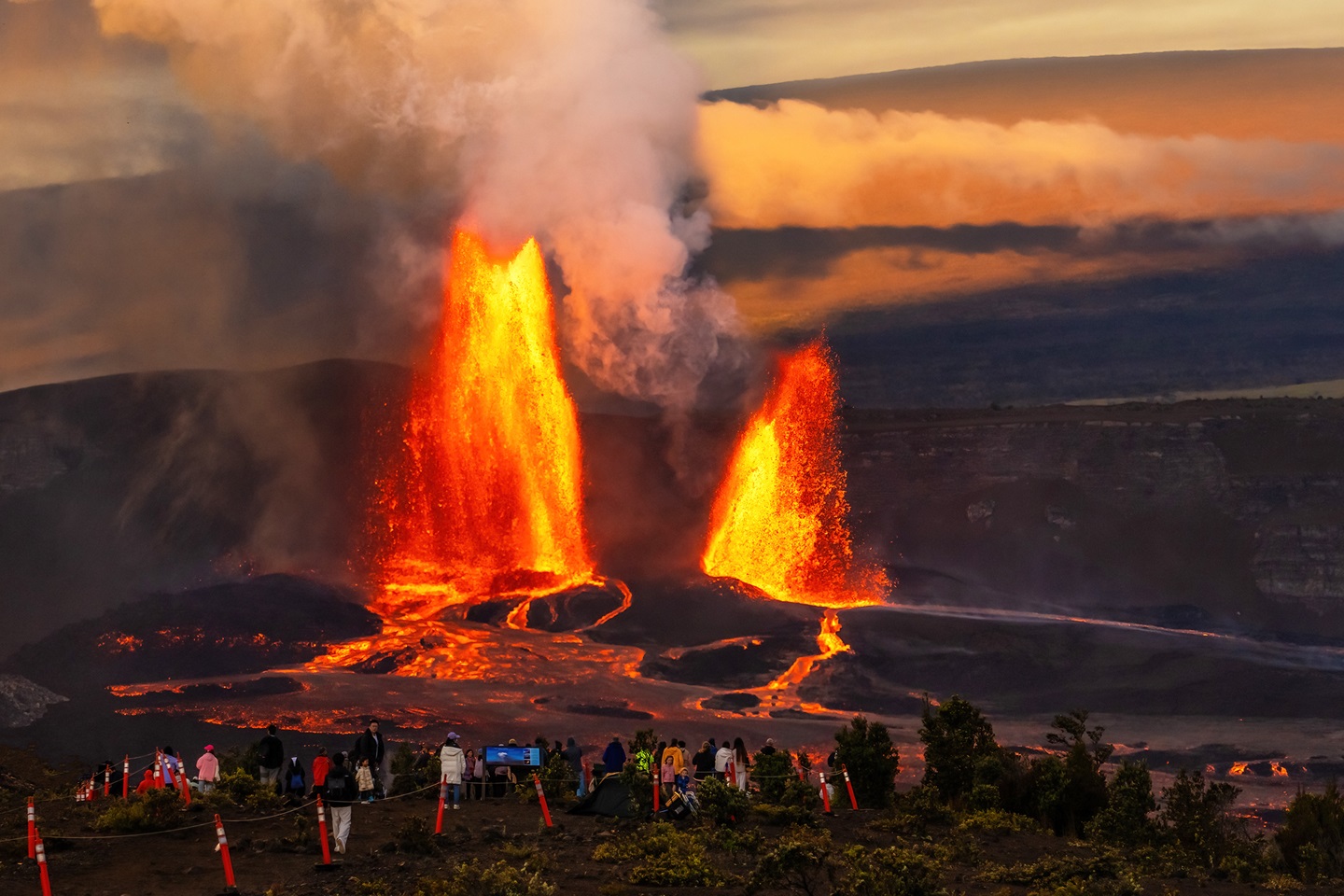 Two fountains of lava erupt from a volcano as visitors watch from a safe distance
