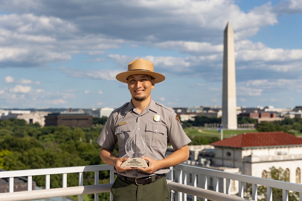 960-NPS_20240821_HVNP-Michael-Newman-in-DC-with-award A park ranger standing outside the Washigton Monument holds an award