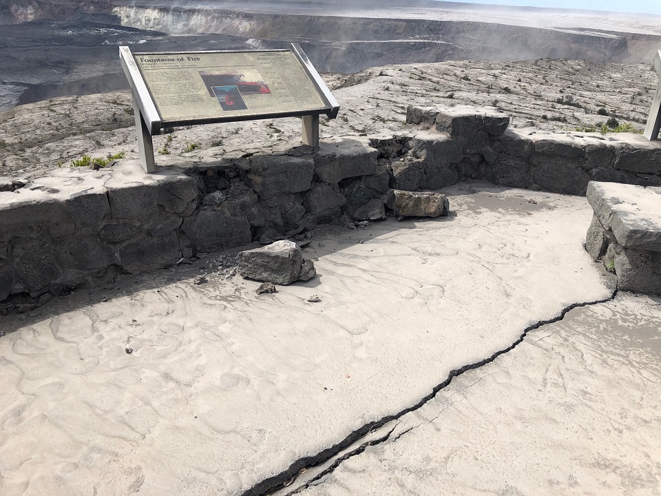 960_Deep crack at Jaggar Museum Overlook_NPS_Photo Image of concrete overlook coated in thick gray volcanic ash and a sign that reads "Fountains of Fire" on a broken rock wall. A long crack is seen on the ground