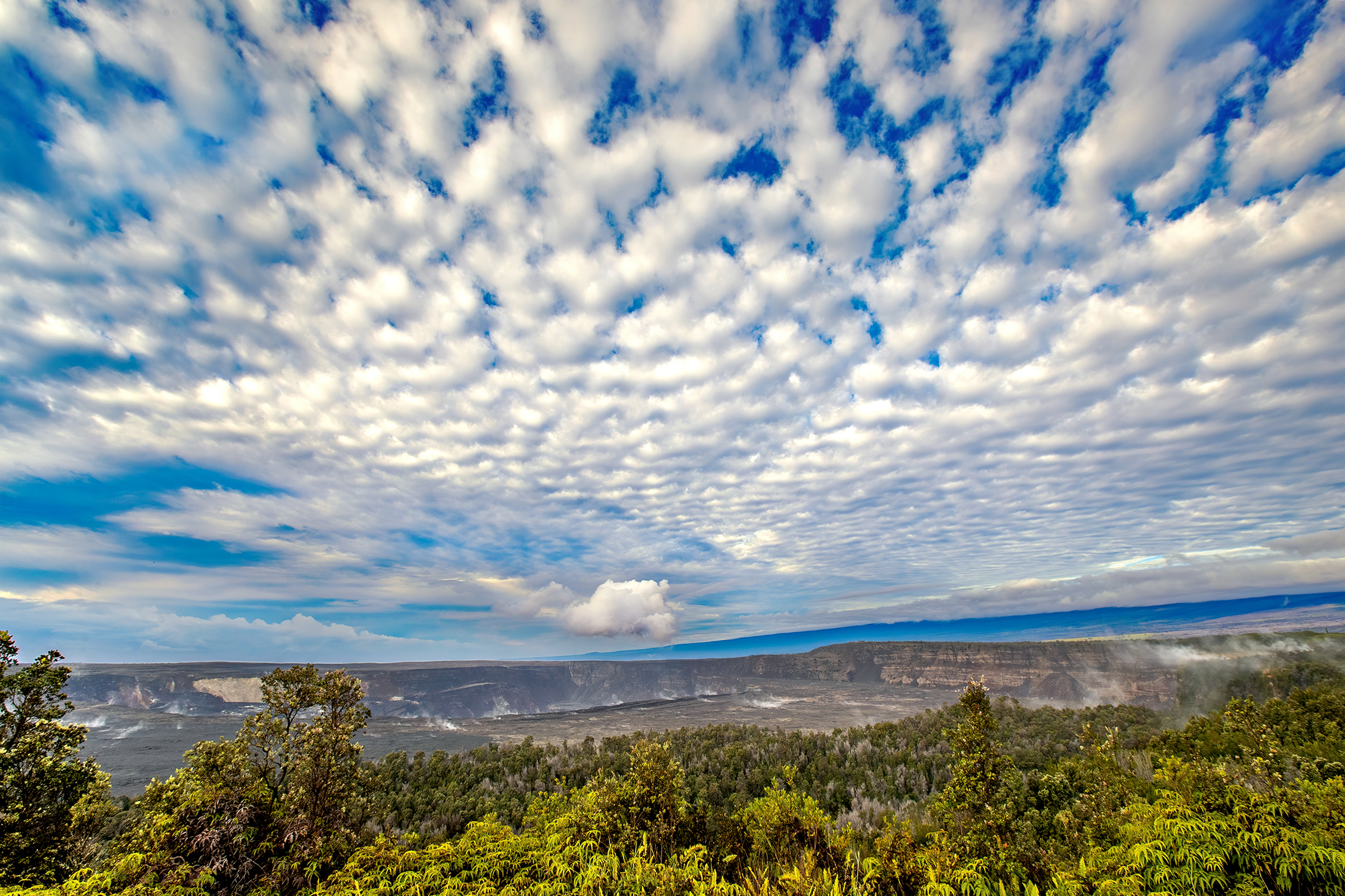 Sheets of white clouds in a blue sky over a wide non-erupting volcano crater