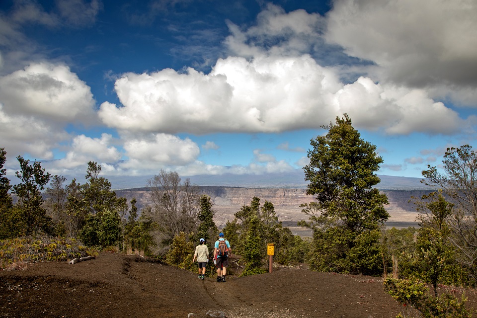 A family hikes Devastation Trail Two people hiking towards a downslope trail, blue sky, clouds and plants