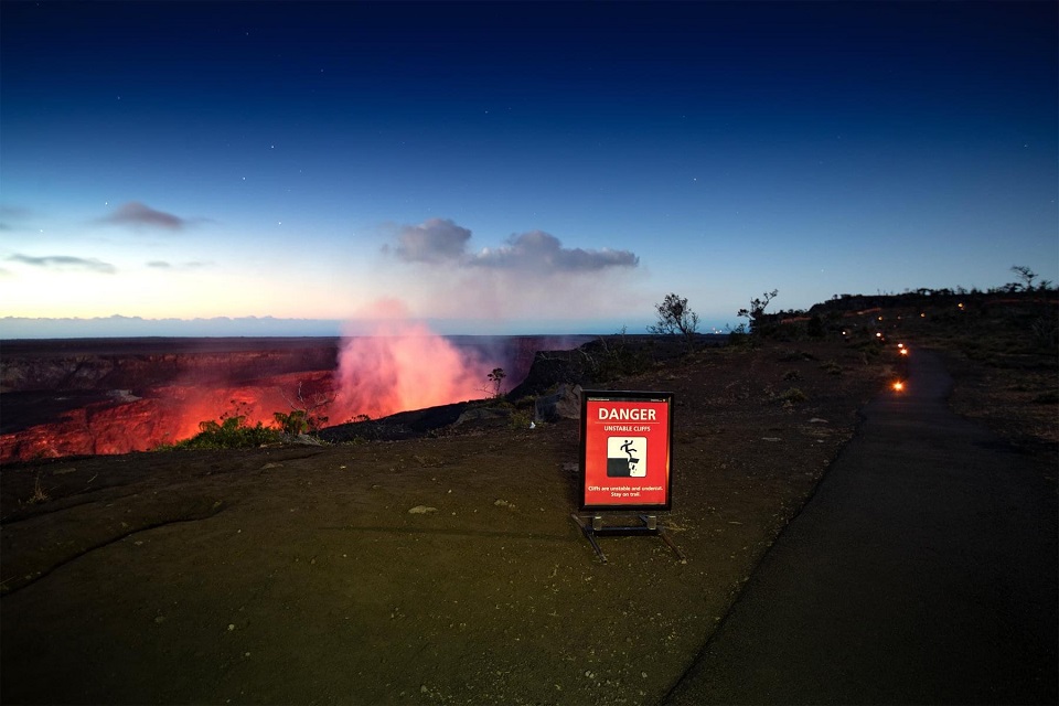 Dangerous cliffs sign near edge of glowing volcano at dawn