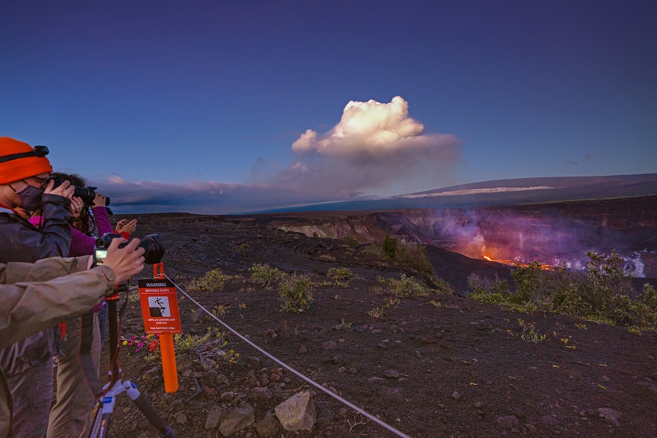 A group of people with cameras pointed at a lava lake about a mile away