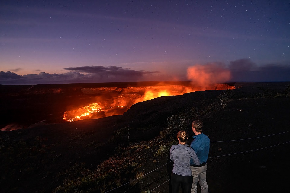 A couple watches a volcanic eruption feed a giant lava lake in the dark
