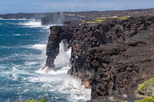 Waves break on a blackish lava rock sea arch