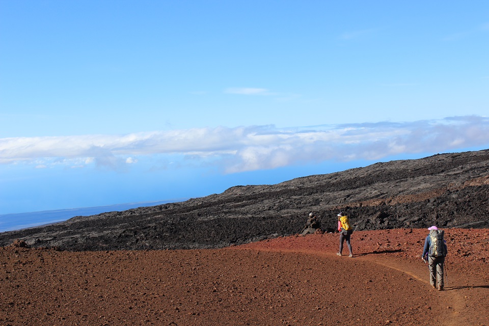 2 hikers walk down a trail of barren lava rock