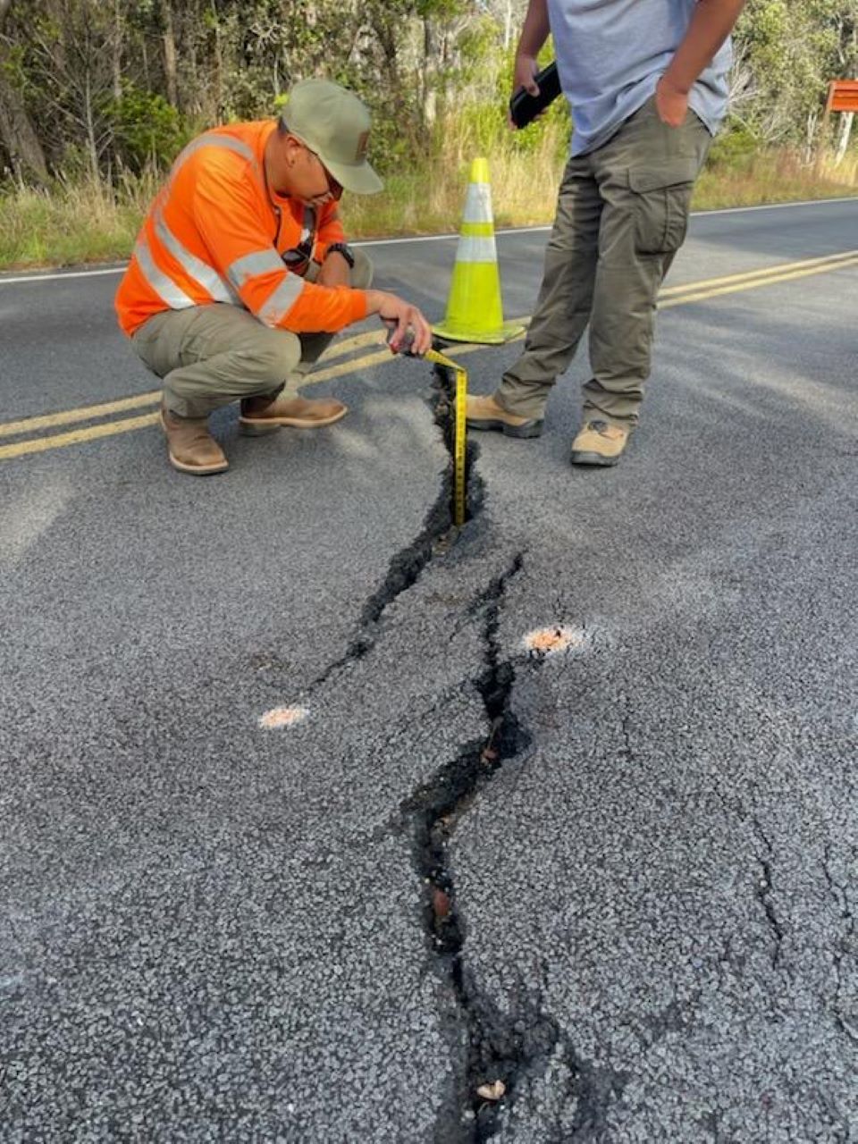 Widened cracks prompt closure of Chain of Craters Road. Workers lowering measuring tape into crack in asphalt road