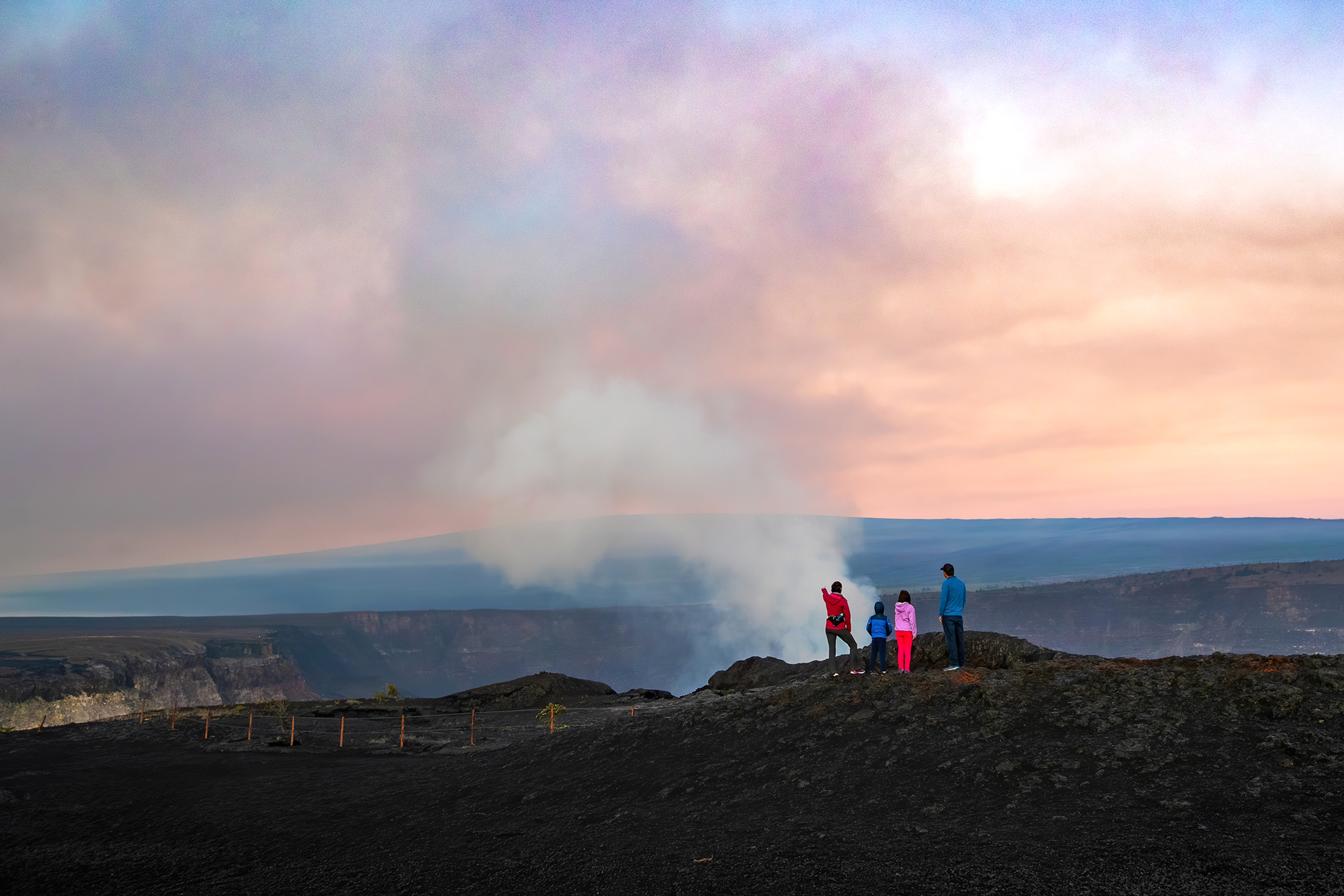 Family at a viewpoint overlooking a steaming volcanic crater at sunrise